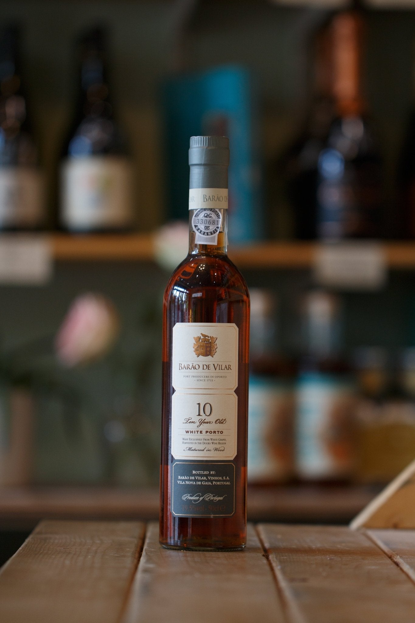 Barão De Vilar 10-Year-Old White Port bottle on a wooden table, showcasing its velvety texture and dried fruit aroma. This exquisite 10 year old white port produced in Portugal features grapes like CÓDEGA DO LARINHO, MALVASIA FINA, and RABIGATO, perfect for sweet and fortified wine lovers.