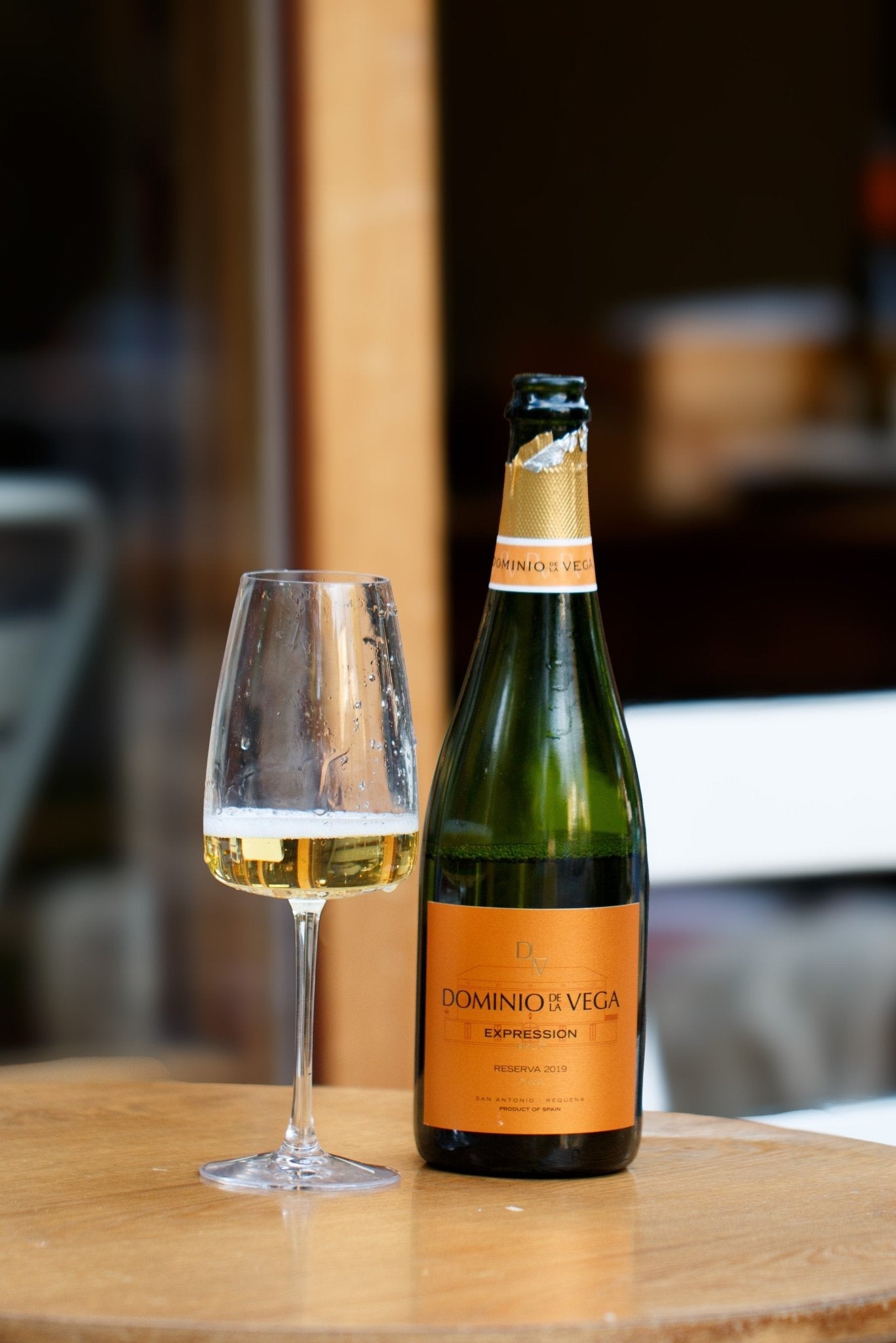 Cava Reserva 2019 from Dominio de la Vega next to an empty glass on a wooden surface, creating a inviting atmosphere perfect for enjoying this vegan-friendly sparkling wine.