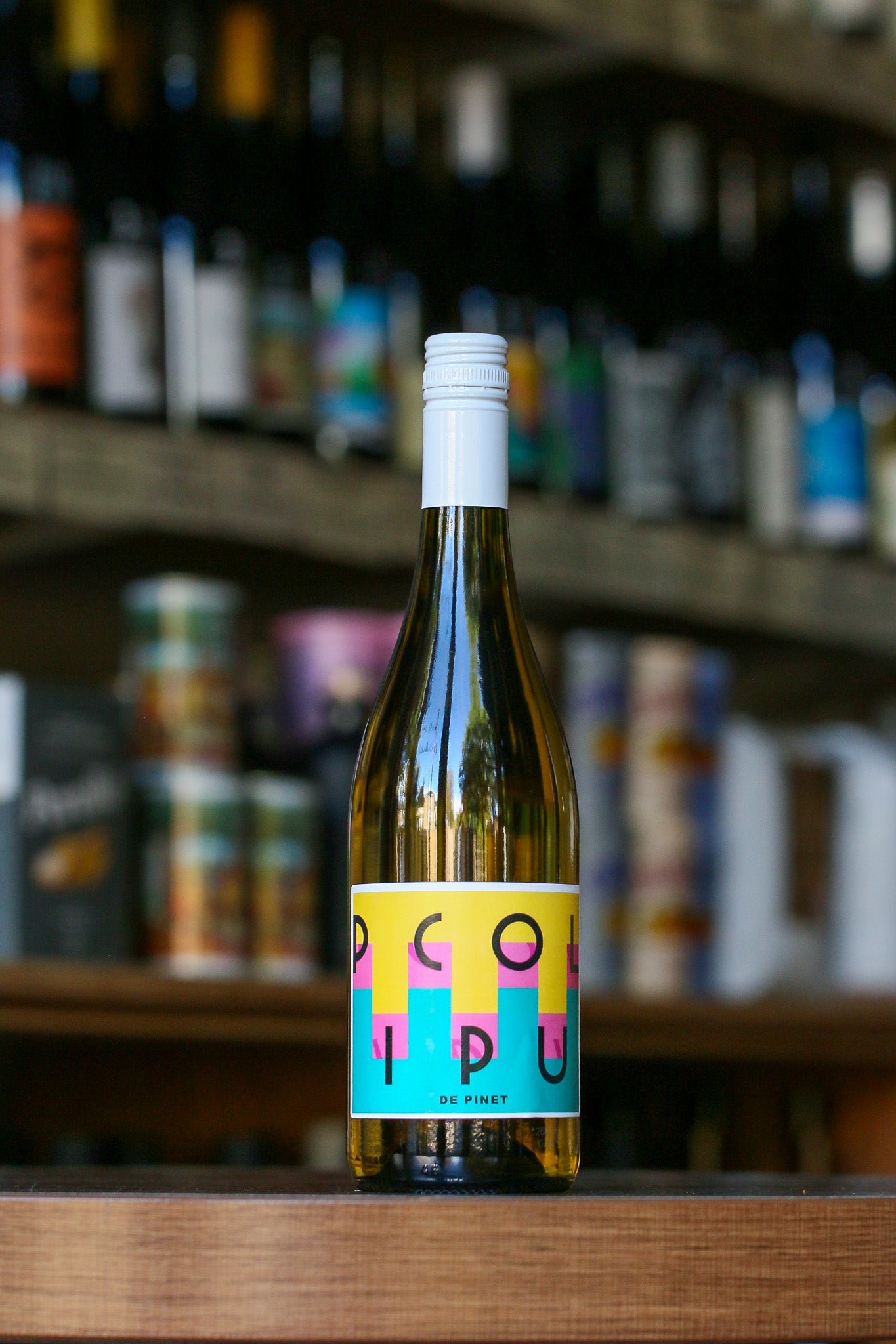 Bottle of Pico Pipo wine on a wooden surface with a blurred background of shelves.