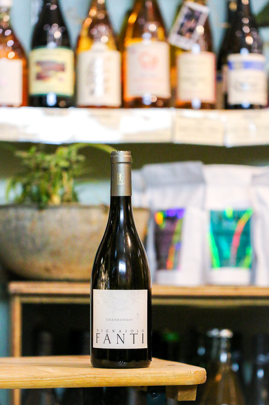 Bottle of Fanti white wine on a wooden surface with shelves of wine bottles in the background