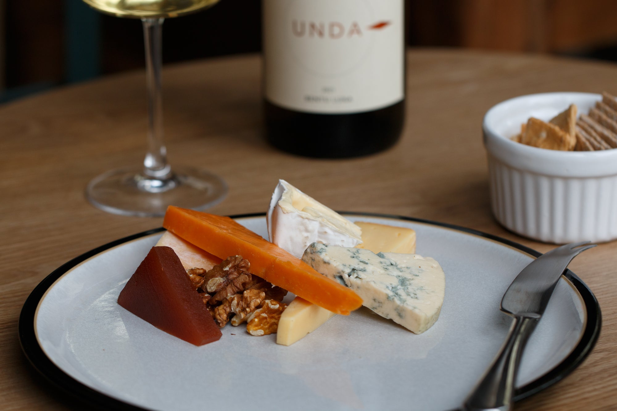 Plated cheeseboard with a glass of wine and bottle on a wooden table
